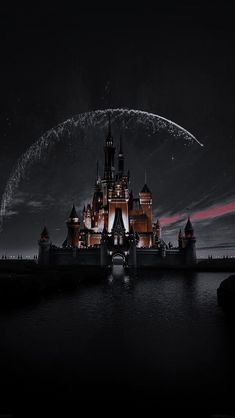 a castle lit up at night with fireworks in the sky above it and water below