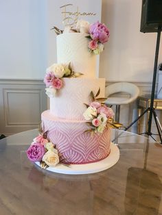 a three tiered wedding cake with pink and white flowers on the top, sitting on a table