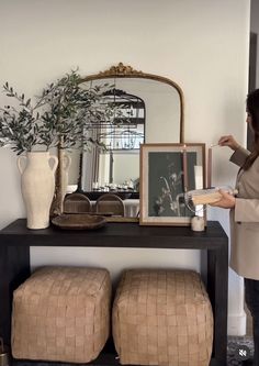 a woman standing in front of a table with two stools and a mirror on it