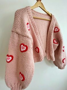 a pink sweater with hearts on it hanging from a wooden hanger next to a white wall