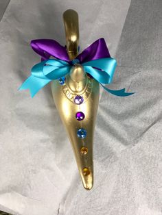 a gold vase with blue and purple ribbons on it's side, sitting on a white sheet