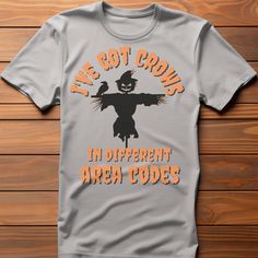 "Introducing our hilarious and quirky Halloween t-shirt that's sure to turn heads and elicit a good laugh! Prepare to sow some laughter this spooky season with our \"I've got crows in different area codes\" t-shirt, featuring an adorably mischievous scarecrow front and center. Crafted from premium, soft cotton, our t-shirt guarantees a comfortable fit that'll keep you at ease whether you're trick-or-treating, attending a costume party, or just enjoying the spooky vibes. The fabric ensures breathability and durability, making it perfect for all your Halloween adventures. Get ready to spread the joy - order yours today and get set to sow some laughter!" Novelty T-shirt With Funny Print For Fall, Funny Cotton Halloween T-shirt, Funny Halloween T-shirt With Screen Print, Halloween Novelty Tops With Funny Text, Halloween Fun T-shirt With Funny Text, Funny Halloween Tops With Text, Funny Halloween T-shirt With Short Sleeves, Funny Halloween T-shirt With Text Print, Funny Halloween T-shirt With Letter Print