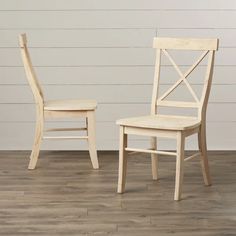 two wooden chairs sitting next to each other on top of a hard wood floor in front of a white wall