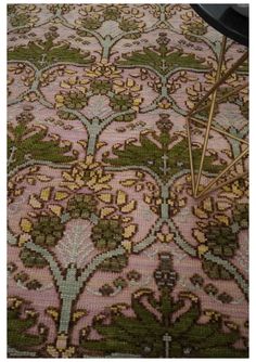 a pink and green rug with gold trimmings on the floor next to a black table