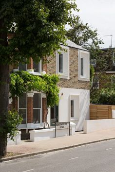 a house with white walls and windows next to a tree on the side of the road