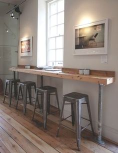 a long counter with stools in front of it on a wooden floor next to a window