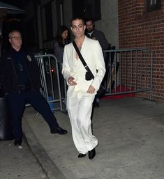 a man in a white suit is walking down the street with his hand on his hip