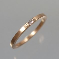 a yellow gold ring with a baguette diamond set in the middle, on a grey background