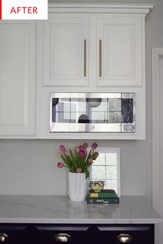 a kitchen with white cabinets and pink flowers in a vase on the counter next to a microwave