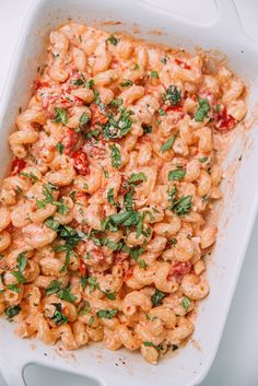 a white casserole dish filled with pasta and garnished with fresh herbs