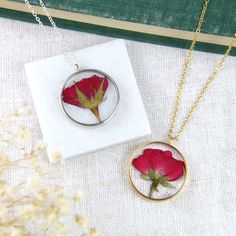 two necklaces with red flowers in them on a white tablecloth next to a book