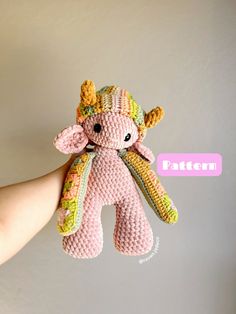 a hand holding a pink stuffed animal with yellow and green decorations on it's face