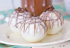 three white chocolate covered desserts on a plate with a cup of coffee in the background