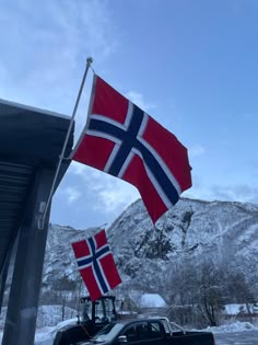 a truck parked next to a flag on top of a pole in the snow with mountains in the background