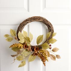 a wreath hanging on the front door with leaves and berries attached to it's sides