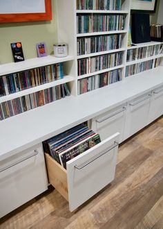 the shelves are filled with various records and cds in white storage drawers, along with other record player's