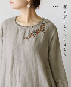 a woman wearing a gray top with orange flowers on the front and side, standing in front of a white wall