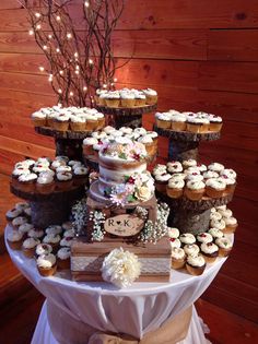 a table topped with lots of cupcakes covered in frosting next to a tree