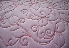 a close up view of a quilted bed with pink and white designs on it