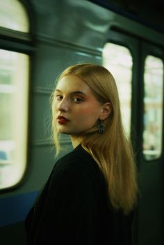 a woman with long blonde hair standing in front of a subway train window, looking out the window