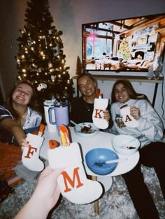 four people sitting at a table with mugs and plates in front of a christmas tree