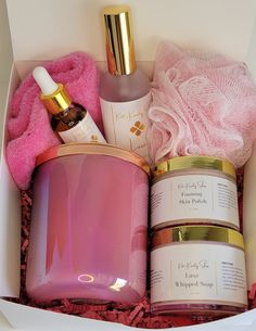 an open gift box containing pink and gold items, such as a candle, body lotion