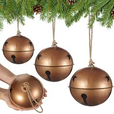 three ornaments hanging from a christmas tree with pine cones in the background and hands holding one ornament