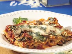 a white plate topped with lasagna covered in mushrooms and spinach sauce on top of a blue table