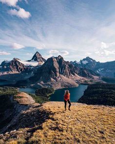 a person standing on top of a grass covered hill with mountains in the back ground