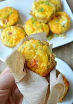 there is a hand holding a small muffin on a plate with other muffins in the background