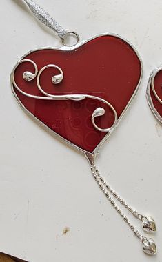 two red heart shaped stained glass ornaments hanging from a chain on a white table top