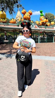 Julia Vaness wearing black linen pants with a white graphic tshirt from Disneyland 2023 Halloween collection, with loungefly mickey mouse bat bag, pumpkin plush earrings, white heart shaped sunglasses and black fuzzy halloween mickey ears Halloween Outfits Casual