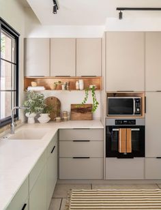 a kitchen with beige cabinets and white counter tops, an area rug and potted plants