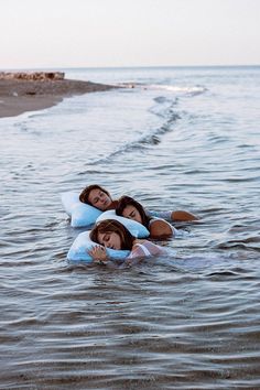 two women are laying on their stomachs in the water while they float down the beach