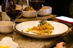 a white plate topped with food next to two glasses of wine