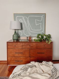 a bedroom with a bed, dresser and plant on top of the dresser in front of it