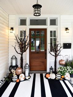 front porch decorated for halloween with black and white striped rug, pumpkins and trees