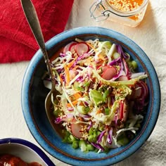 a blue bowl filled with coleslaw and carrots next to another bowl full of dressing