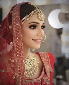 a woman wearing a red and gold bridal outfit with jewelry on her head, smiling at the camera