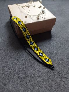 a yellow and blue beaded bracelet sitting on top of a wooden box next to flowers