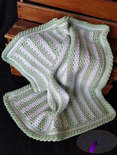 a green and white crocheted blanket sitting on top of a wooden bench next to a black background