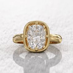 a yellow gold engagement ring with a cushion cut diamond in the center on a white background