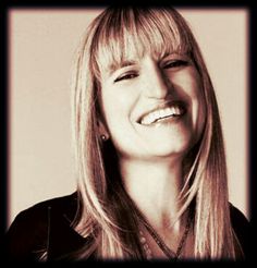 a woman with long blonde hair smiling and wearing a black shirt, necklaces and earrings