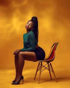 a woman sitting on top of a chair in front of a yellow background with her legs crossed