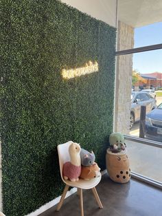 there are stuffed animals sitting on the chair in front of the wall that is covered with green plants