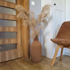 a brown vase with some dry grass in it next to a wooden chair and door