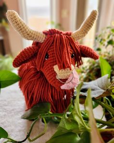 a red stuffed animal sitting on top of a table next to green leaves and plants