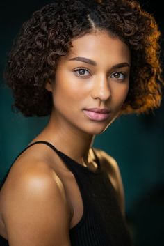 a woman with curly hair is posing for the camera and looking at the camera while wearing a black tank top