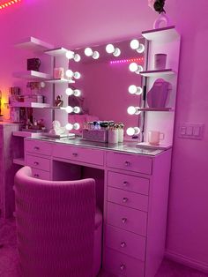 a pink vanity with lights on it and a chair in front of the mirror that is lit up