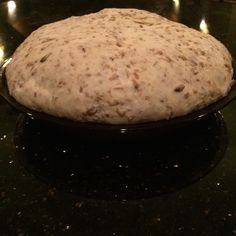 an uncooked pizza dough sitting on top of a black counter with lit candles in the background